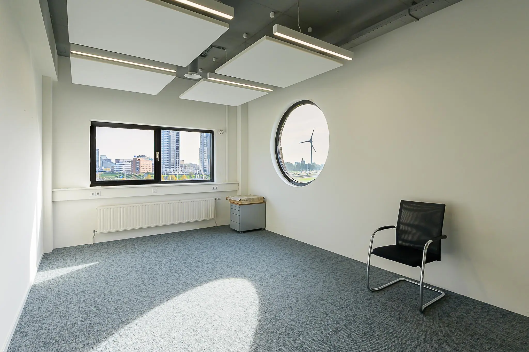 Lichte, lege kantoorruimte aan de K.P. van der Mandelelaan met uitzicht op een windmolen en hoogbouw.